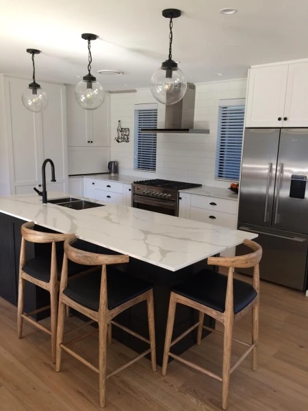 Pale veined island with black cabinetry, timber stools and pendant lighting.